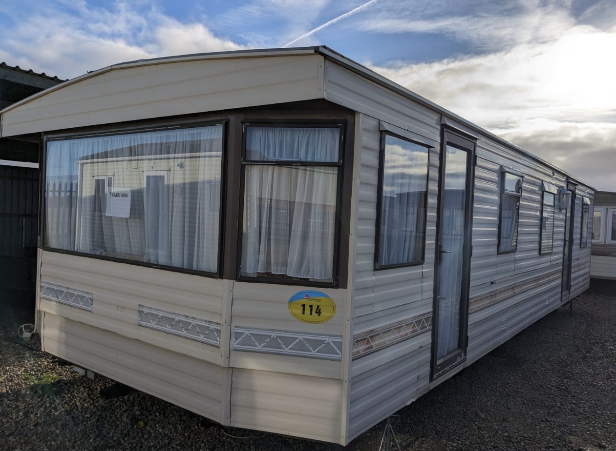 A long used static caravan standing on gravel under a blue sky