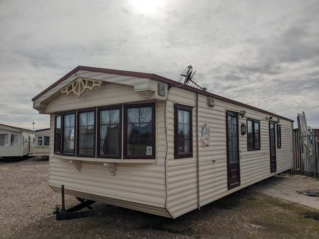 A used static caravan with a decorative gable and bay windows, standing on gravel